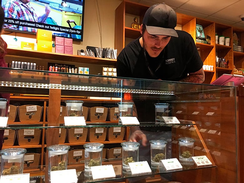 Torrey Holistics employee Taron McElroy arranges jars of cannabis in San Diego, Calif., Thursday, Dec. 14, 2017.